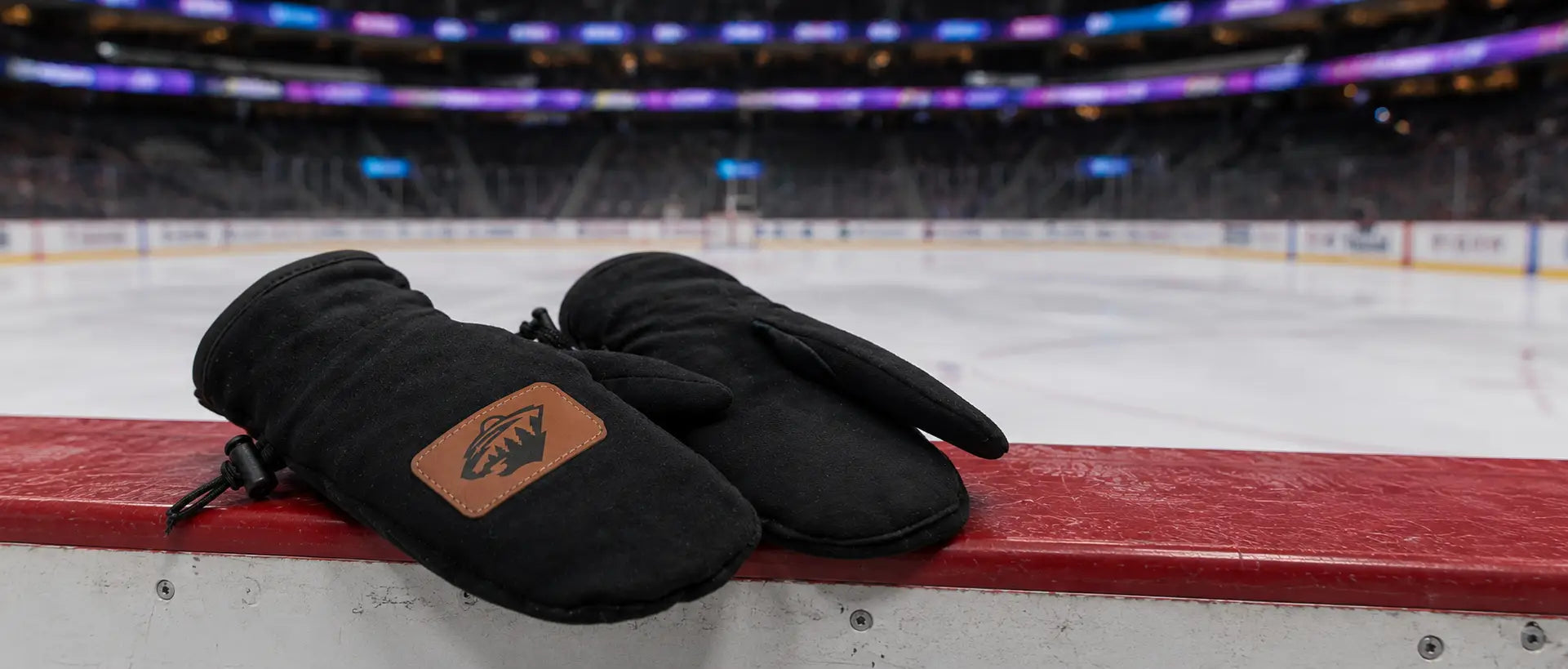 Black mittens with a leather patch on a hockey bench with an ice rink background